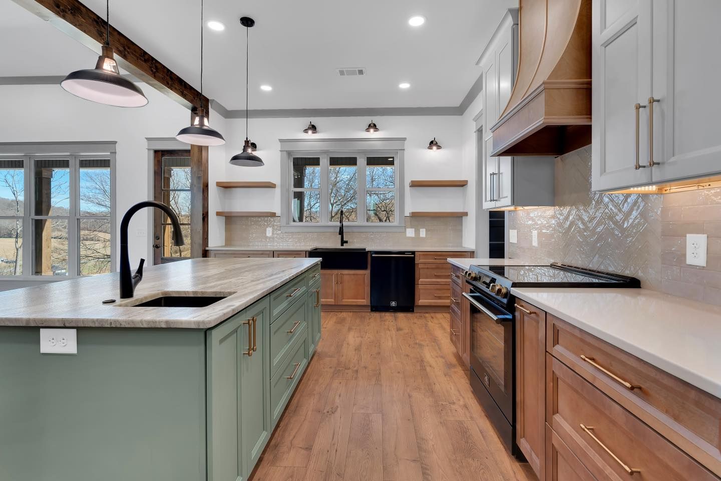A kitchen with green cabinets, wooden floors, stainless steel appliances, and a large island.