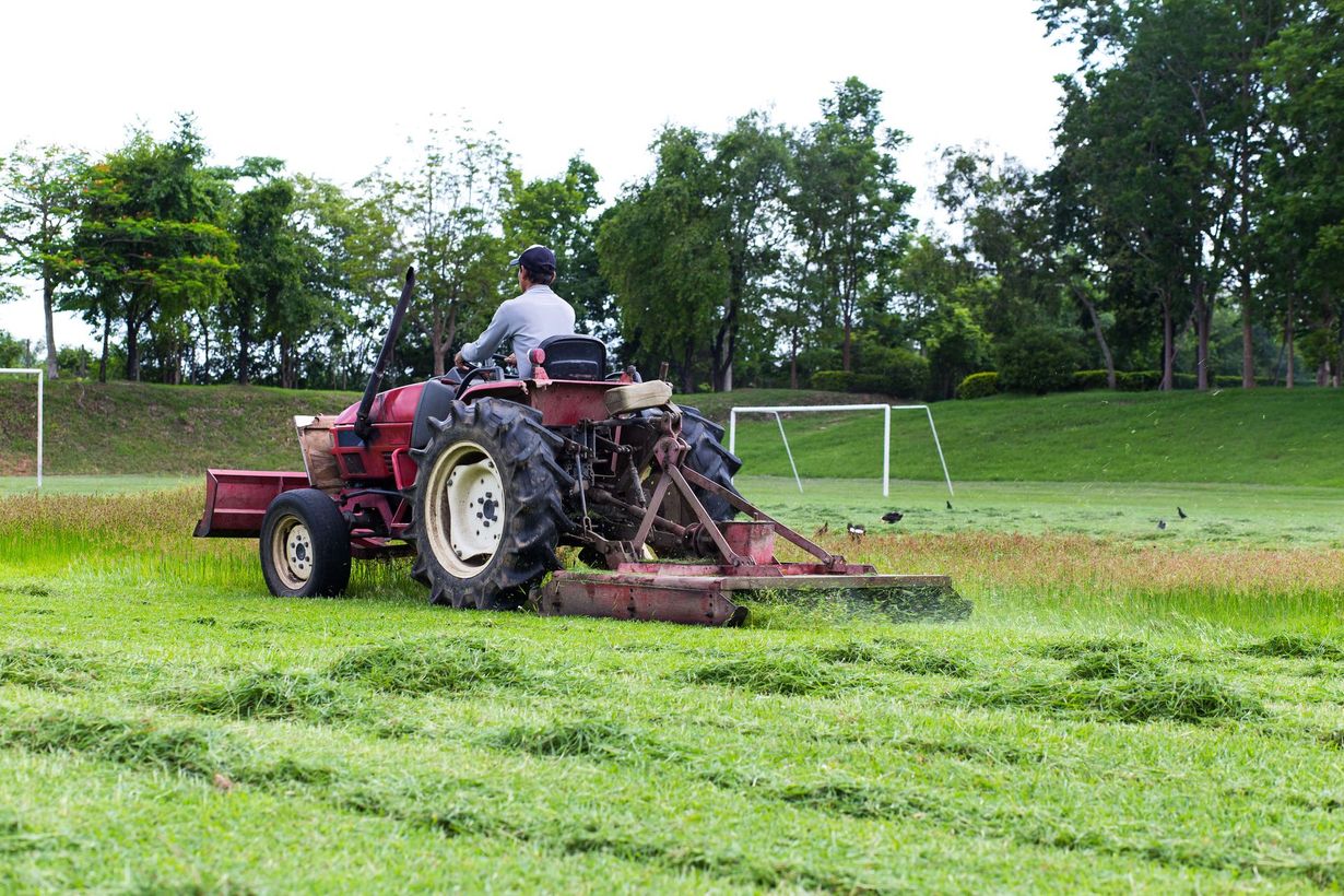 Farmer driving a red tractor mowing grass on a green field near soccer goals