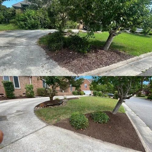 Landscaped corner with curved sidewalk, green grass, trees, and low shrubs beside brick houses.