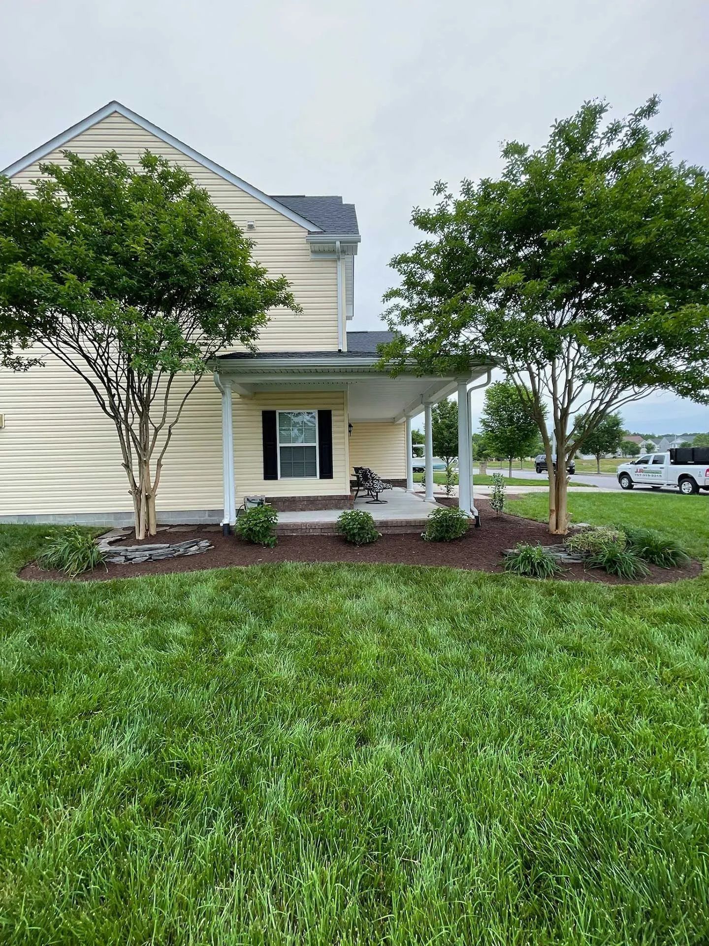 Suburban house with beige siding, covered porch, and landscaped front yard under cloudy sky