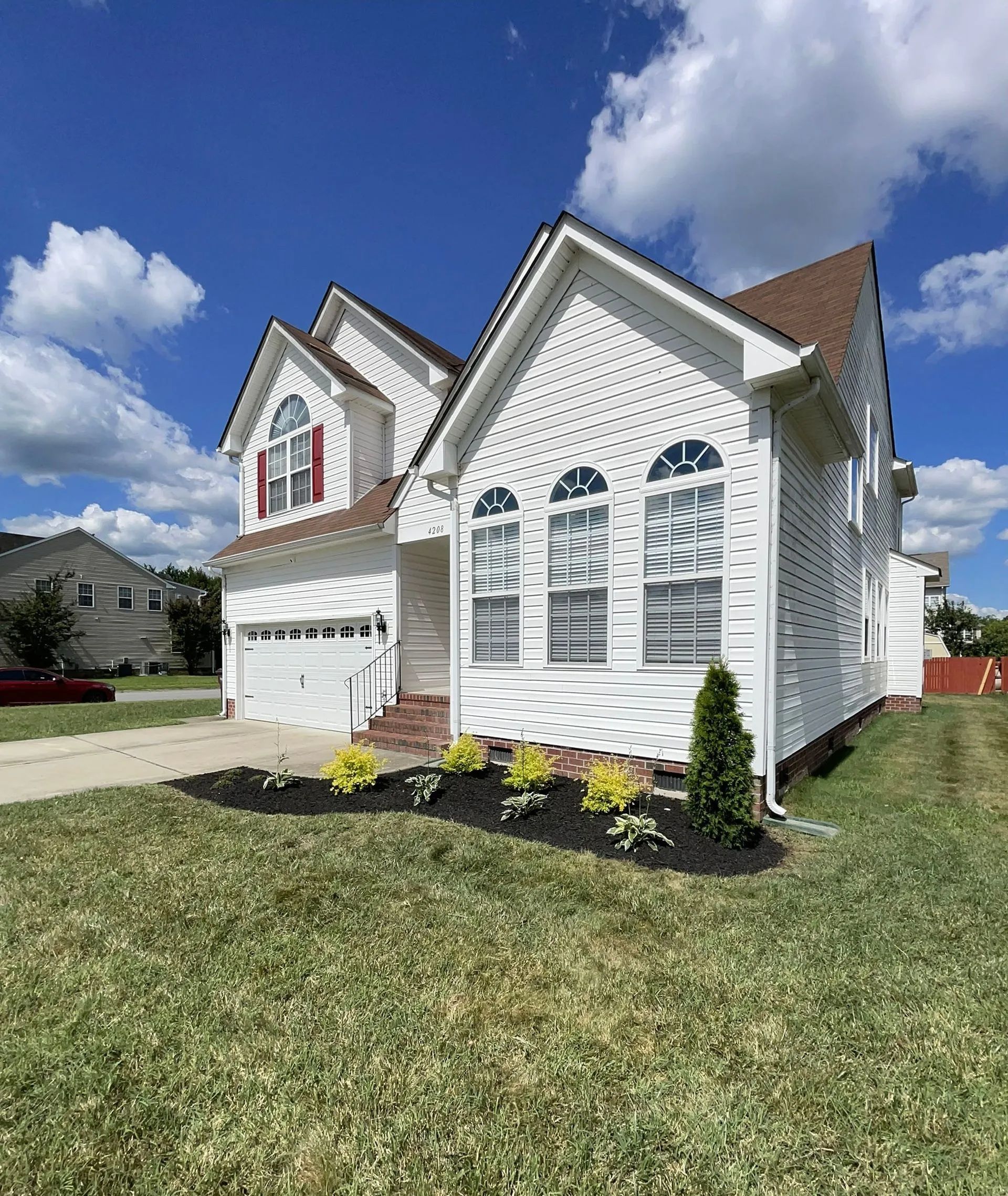 White suburban house with gray shutters, arched windows, front garage, and landscaped lawn under a blue sky