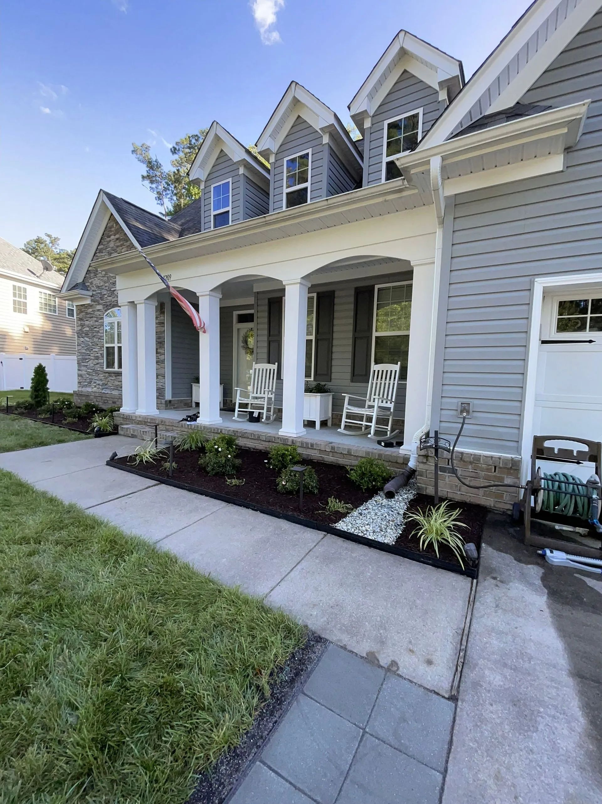 Front porch of a gray townhouse with white trim, potted plants, and a concrete walkway under a blue sky
