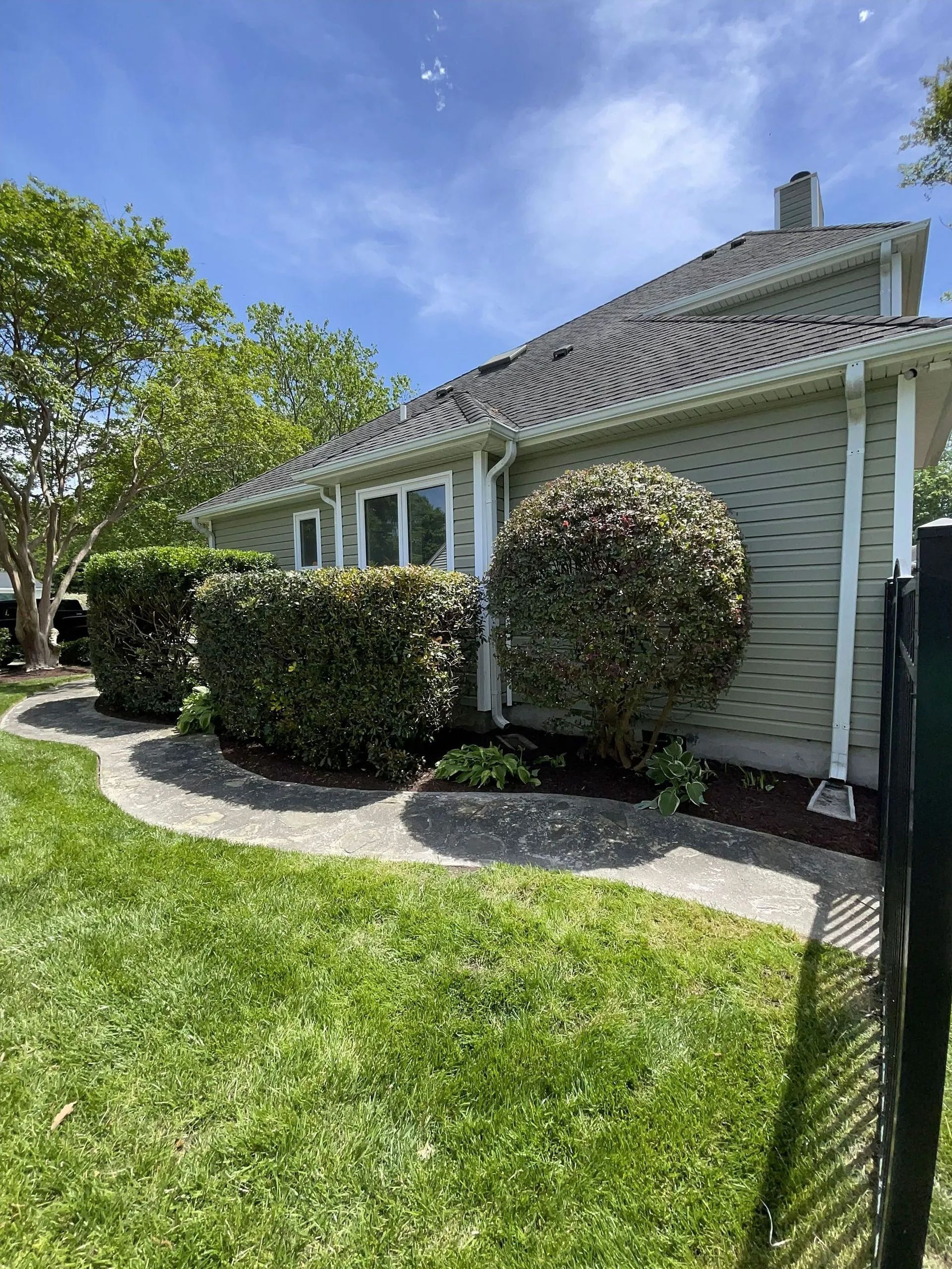 Single-story house with white siding, trimmed hedges, and a green lawn under a blue sky