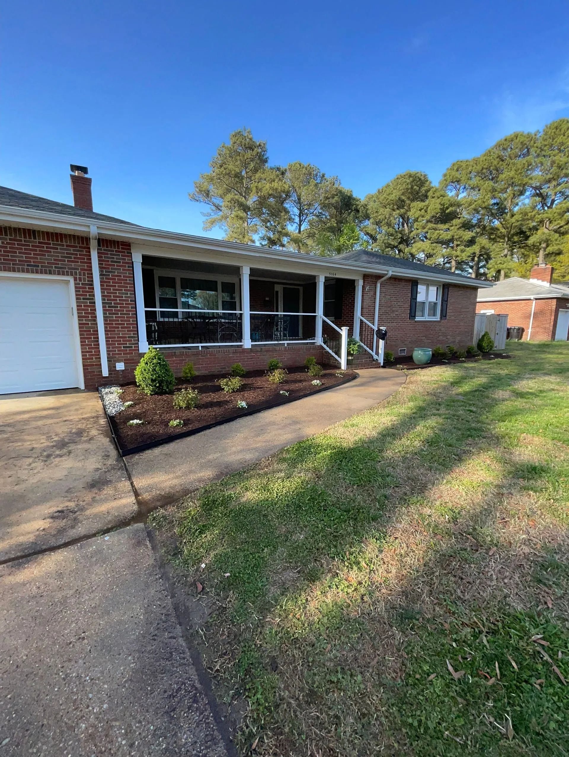 Brick house exterior with white garage door, front porch, and sloped lawn under a blue sky