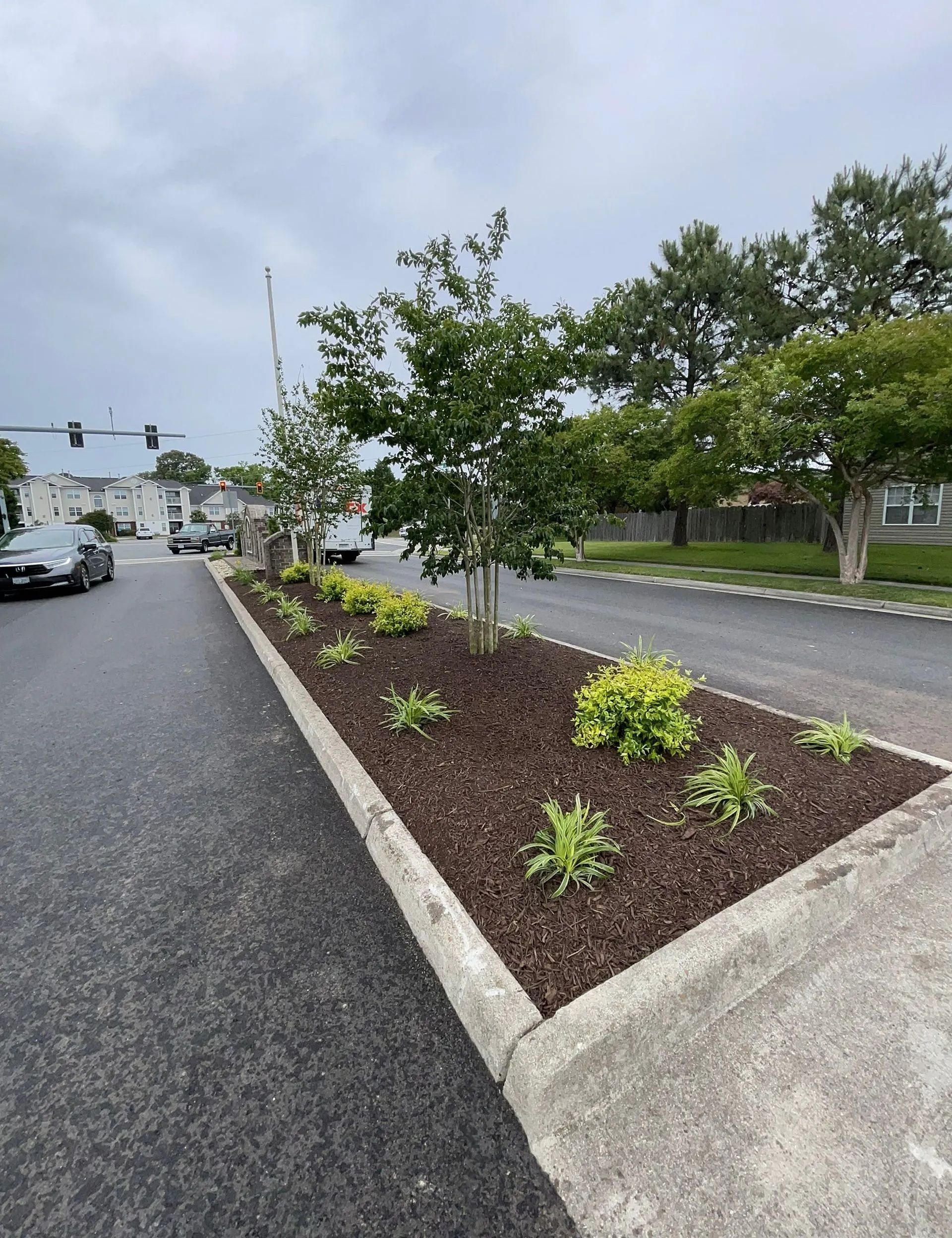 Landscaped median with small shrubs beside a wet road at an intersection on a cloudy day