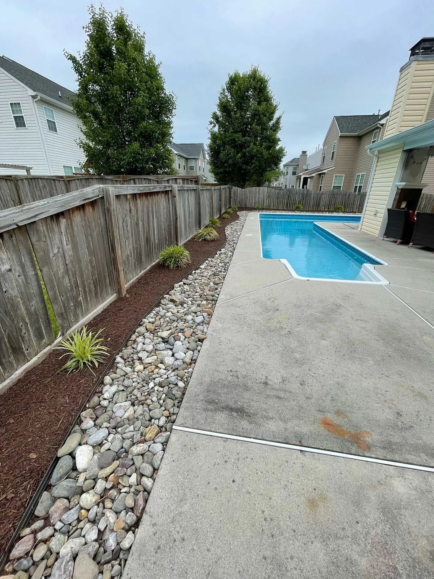 Backyard with a small in-ground pool, concrete patio, wooden fence, and landscaped rock border