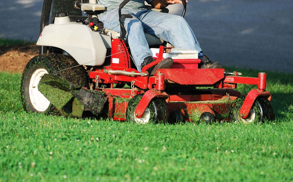 Person mowing a bright green lawn with a red riding mower