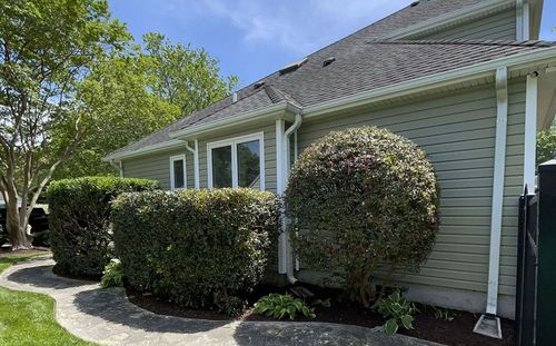 Single-story house with white trim, green siding, and neatly trimmed bushes along the front lawn.