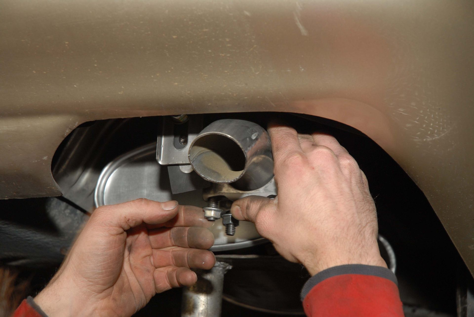 Hands connecting an exhaust pipe to a vehicle's muffler, under a car.