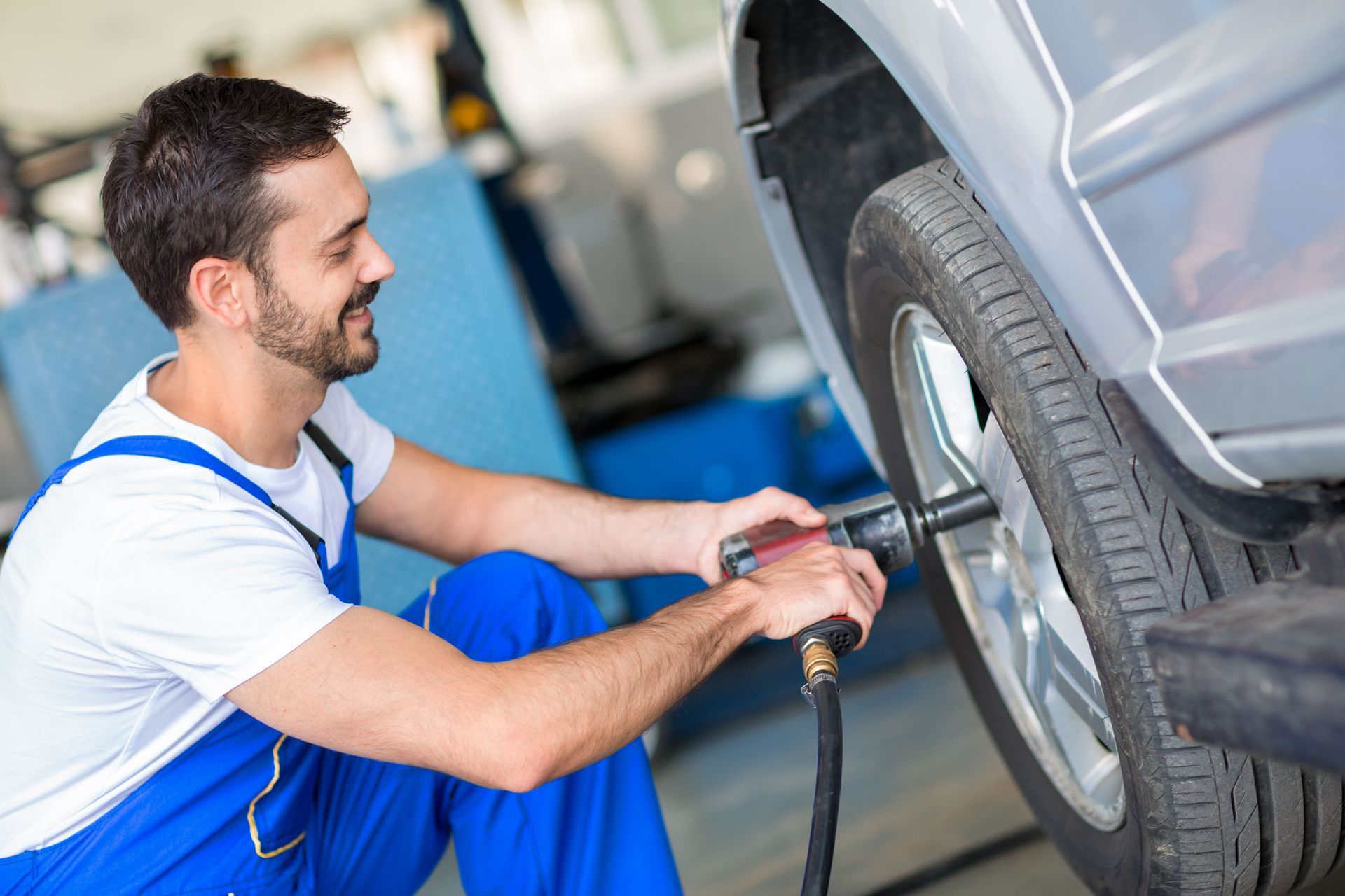 Mechanic using a power tool to tighten lug nuts on a car tire in a garage.
