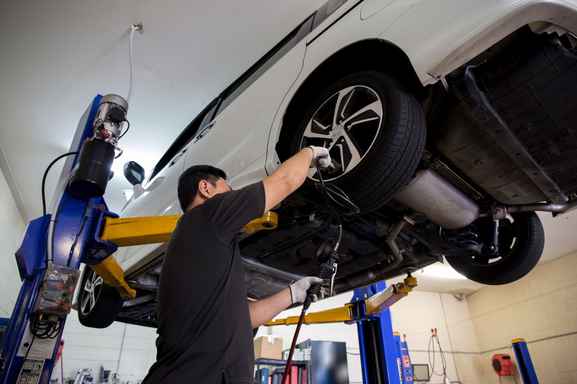 Mechanic working on a white car raised on a lift in a repair shop.