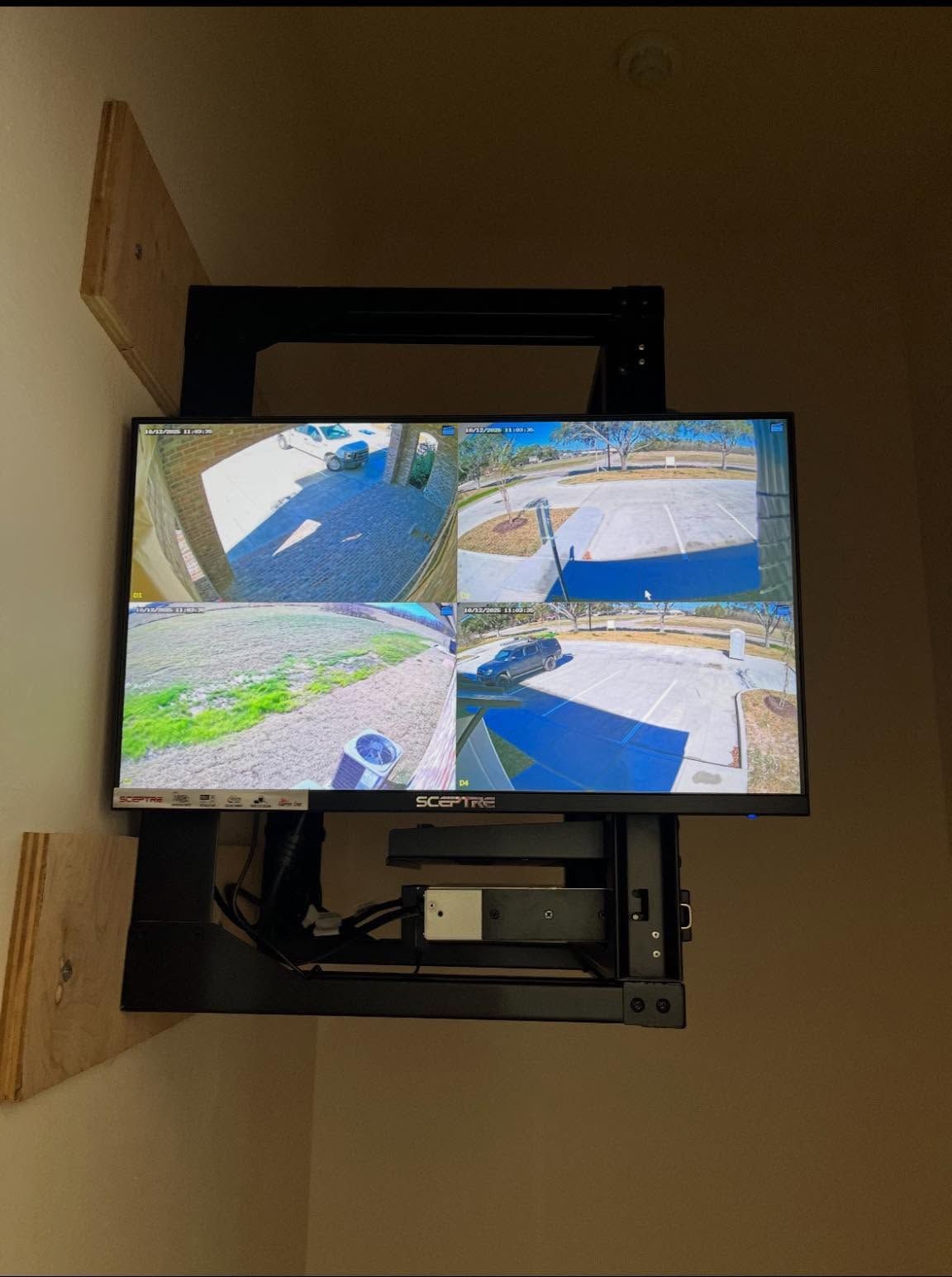 Wall-mounted TV displaying four CCTV camera views of an outdoor driveway and yard area