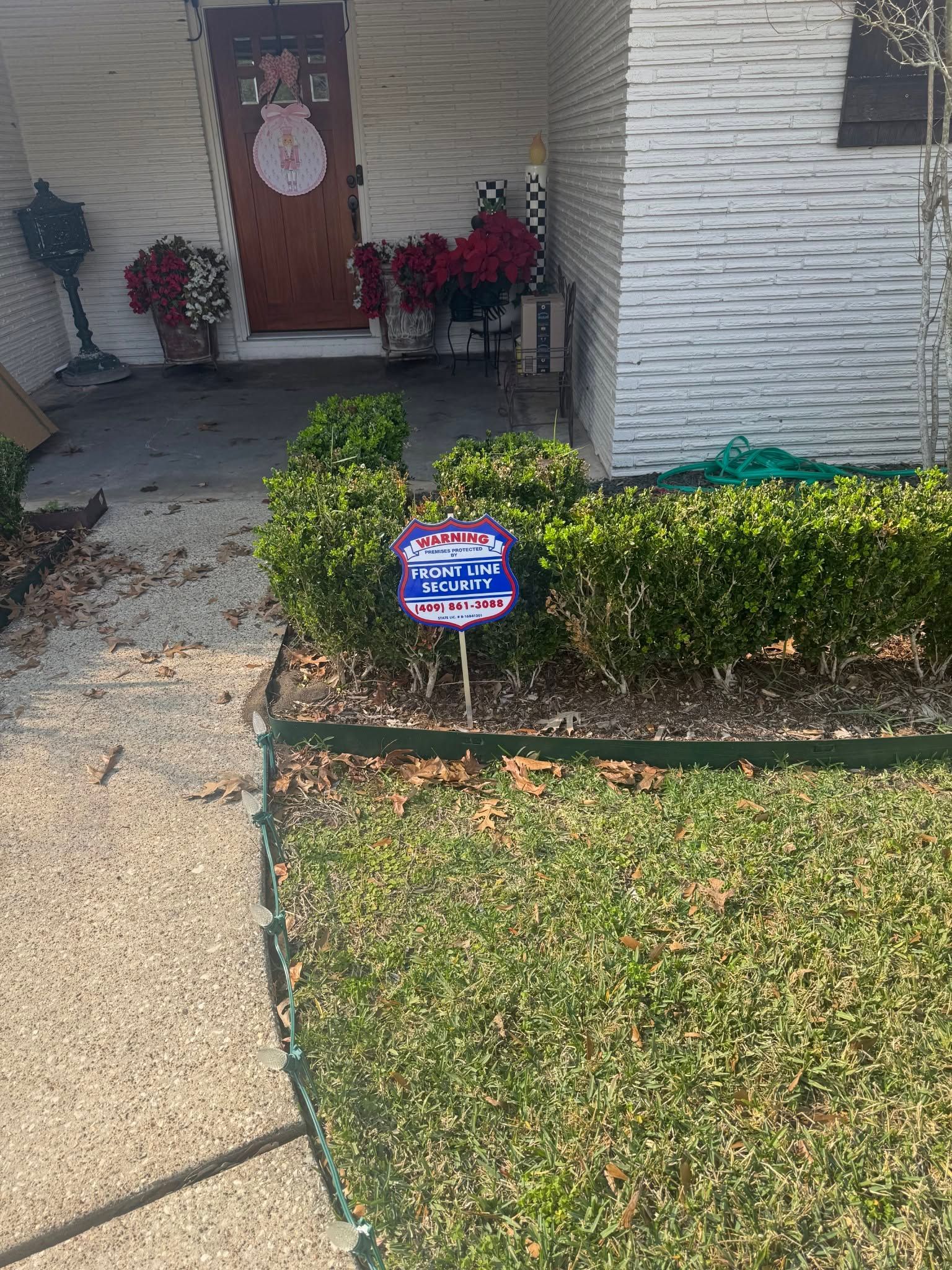 Front yard walkway leading to a red front door, with a trimmed hedge and a small yard sign.