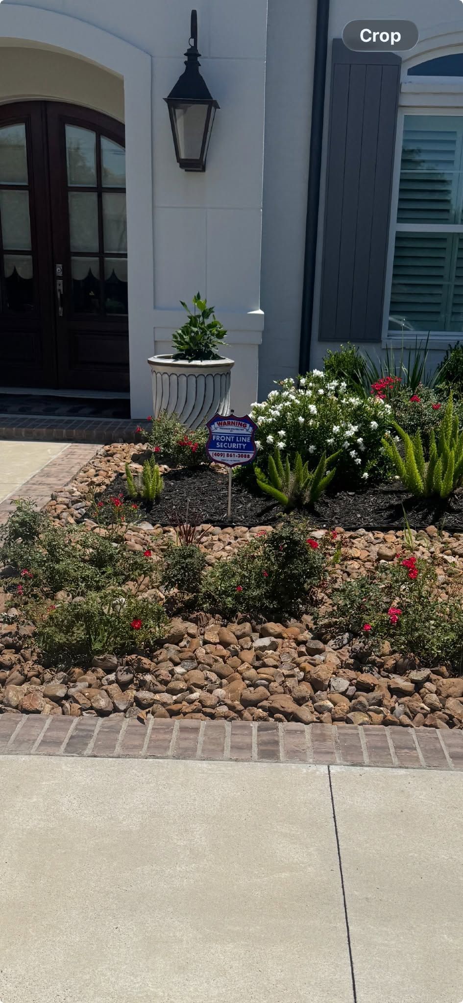Front entrance with white door, blue shutters, lantern, and a rock garden with potted plant and flowers.