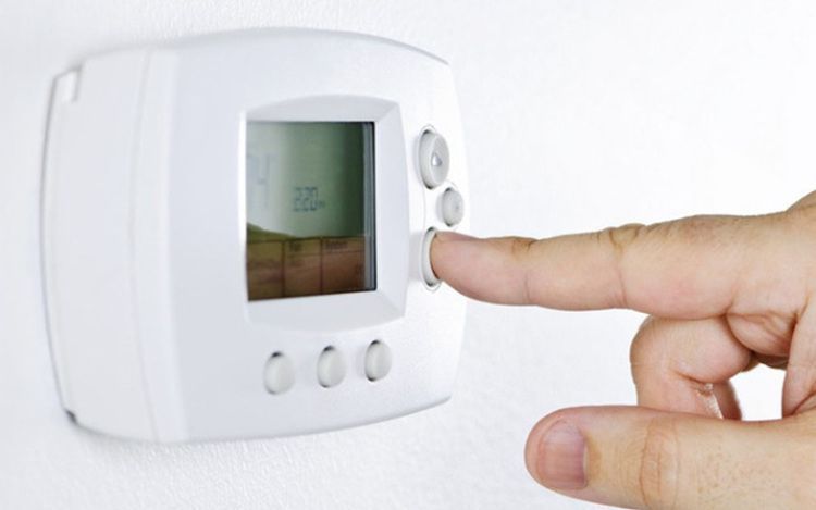A finger pressing a button on a white wall thermostat display.