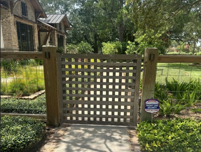 Wooden lattice gate at the entrance to a garden path, surrounded by greenery and flowers.
