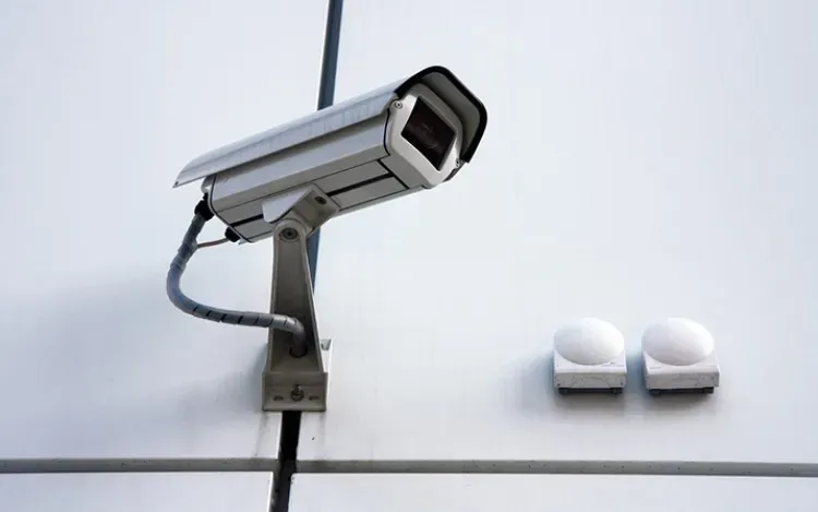 Security camera mounted on a white wall beside two small white wall fixtures.