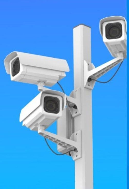 Four white surveillance cameras mounted on a gray pole against a blue sky