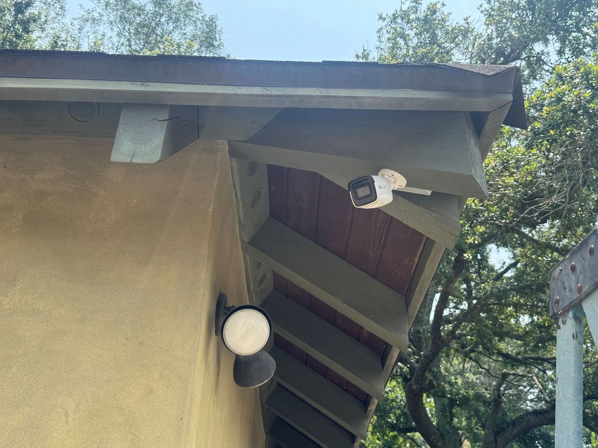 Hands adjusting a white security camera mounted under a metal roof