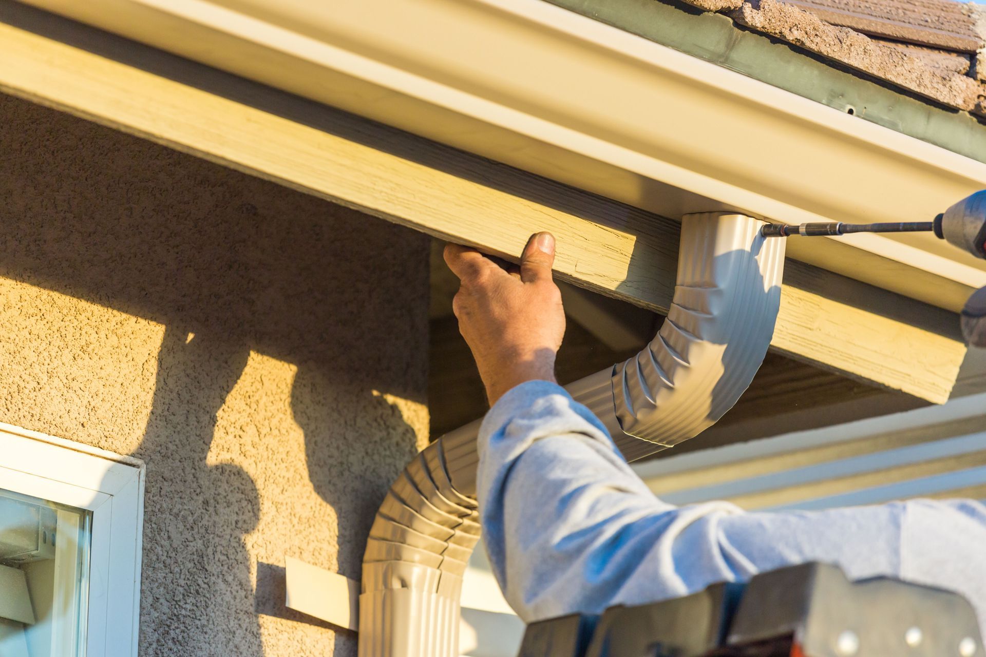 Worker installing gutter on a house exterior under the roof eaves
