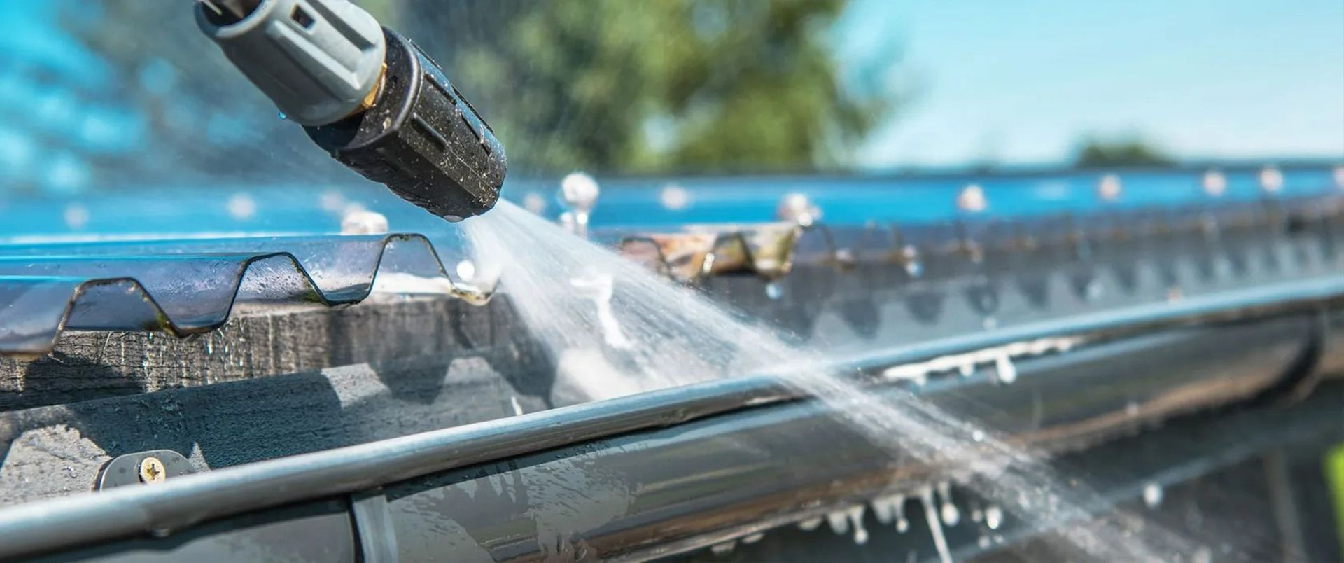 Pressure washer spraying water across a car windshield on a sunny day