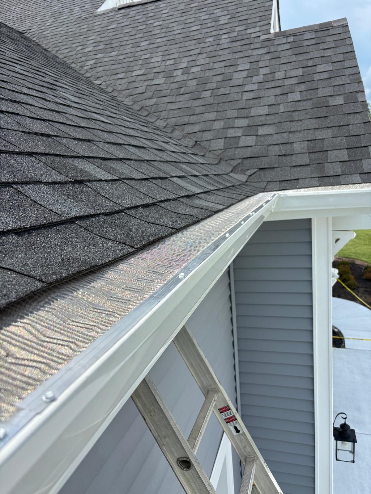 Roofline and white gutter on a house beside gray shingles and an extension ladder.