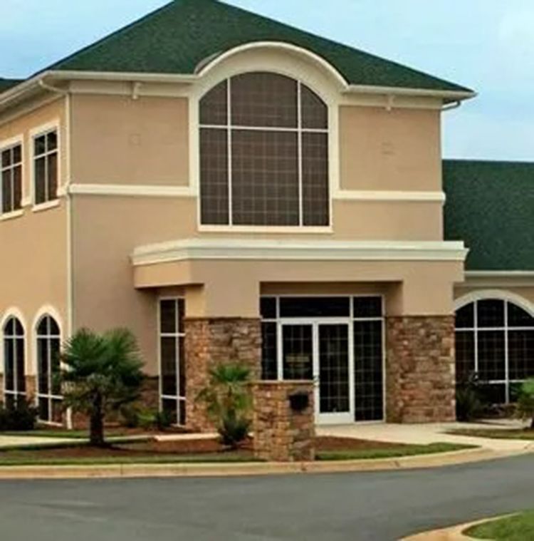 Two-story beige office building with stone accents and large arched windows along a curved driveway