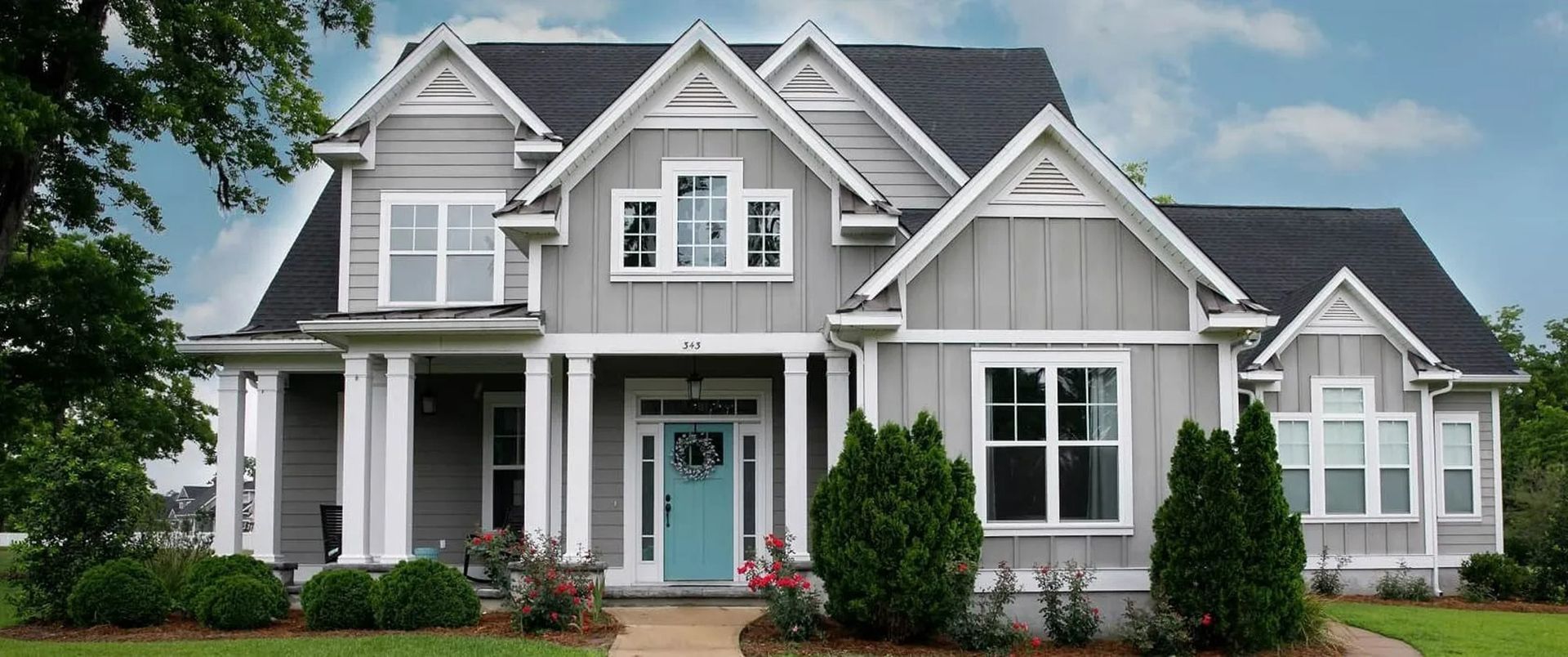 Large gray two-story house with white trim, front porch, and a teal front door