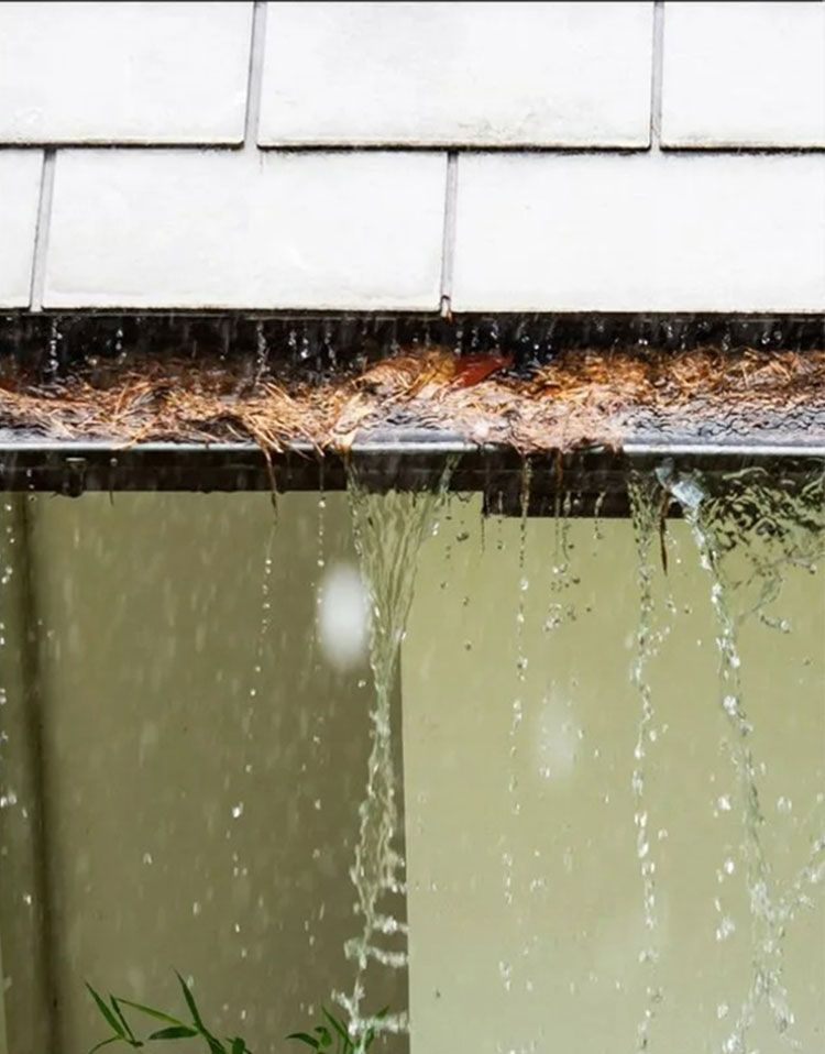 Damaged roof gutter overflowing with water and debris above a green wall
