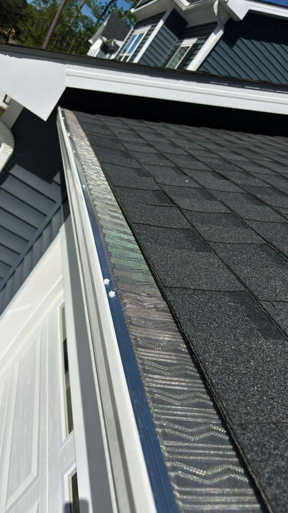 Close-up of a roof edge with gray shingles, white trim, and a rooftop vent in sunlight