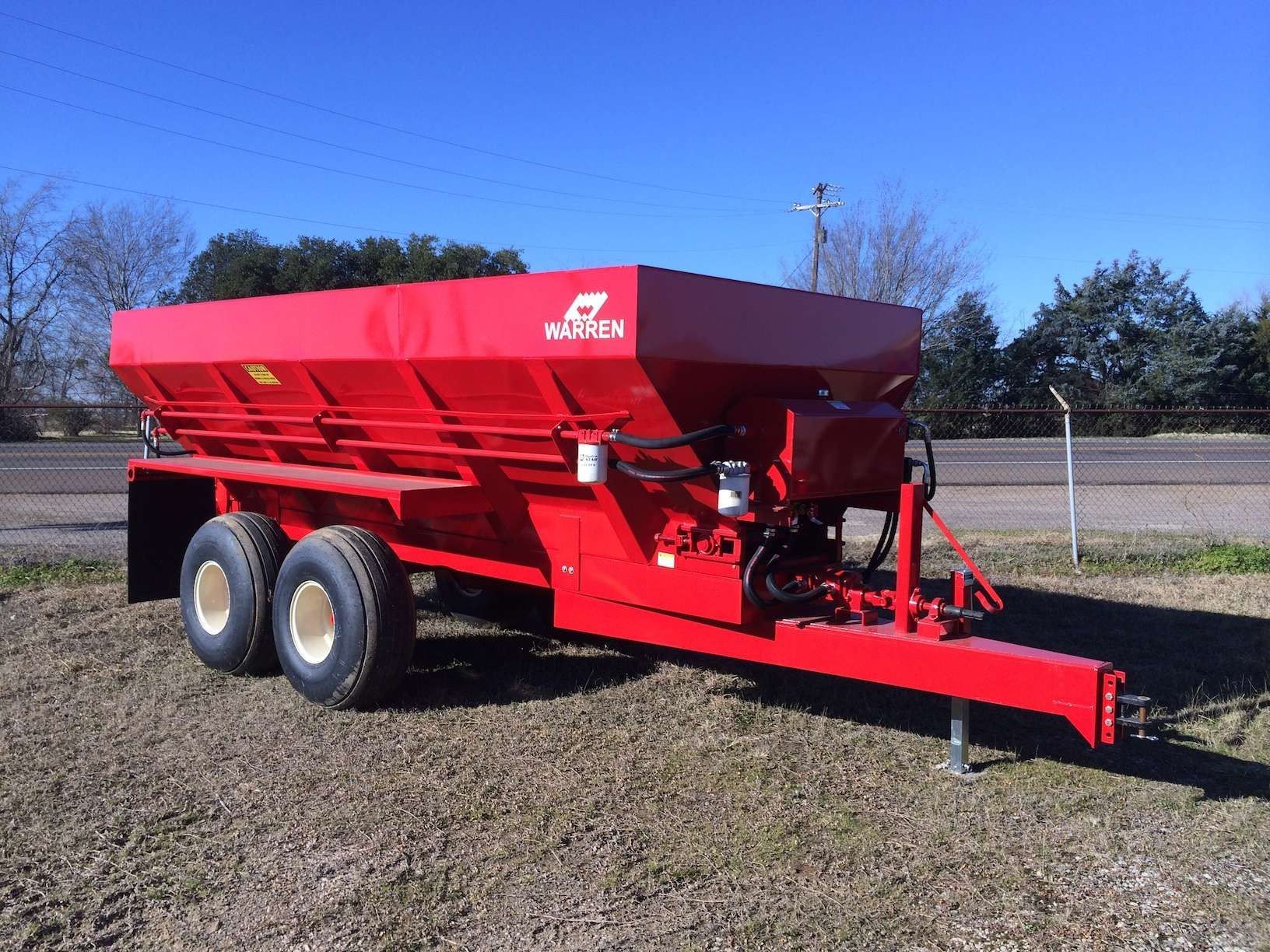 A red trailer is parked in a dirt field next to a road.
