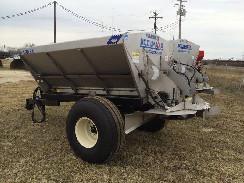 A stainless steel spreader is parked in a field