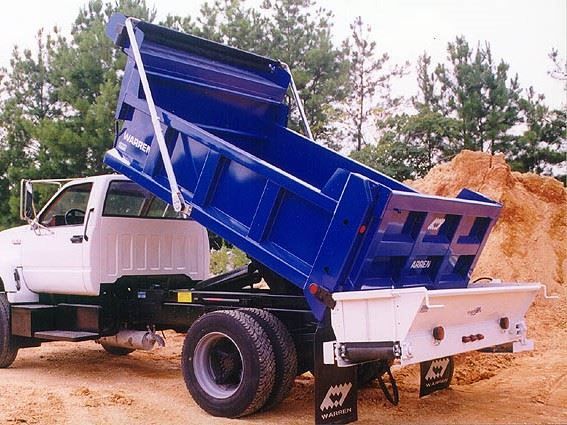A white dump truck with a blue bed is parked in the dirt