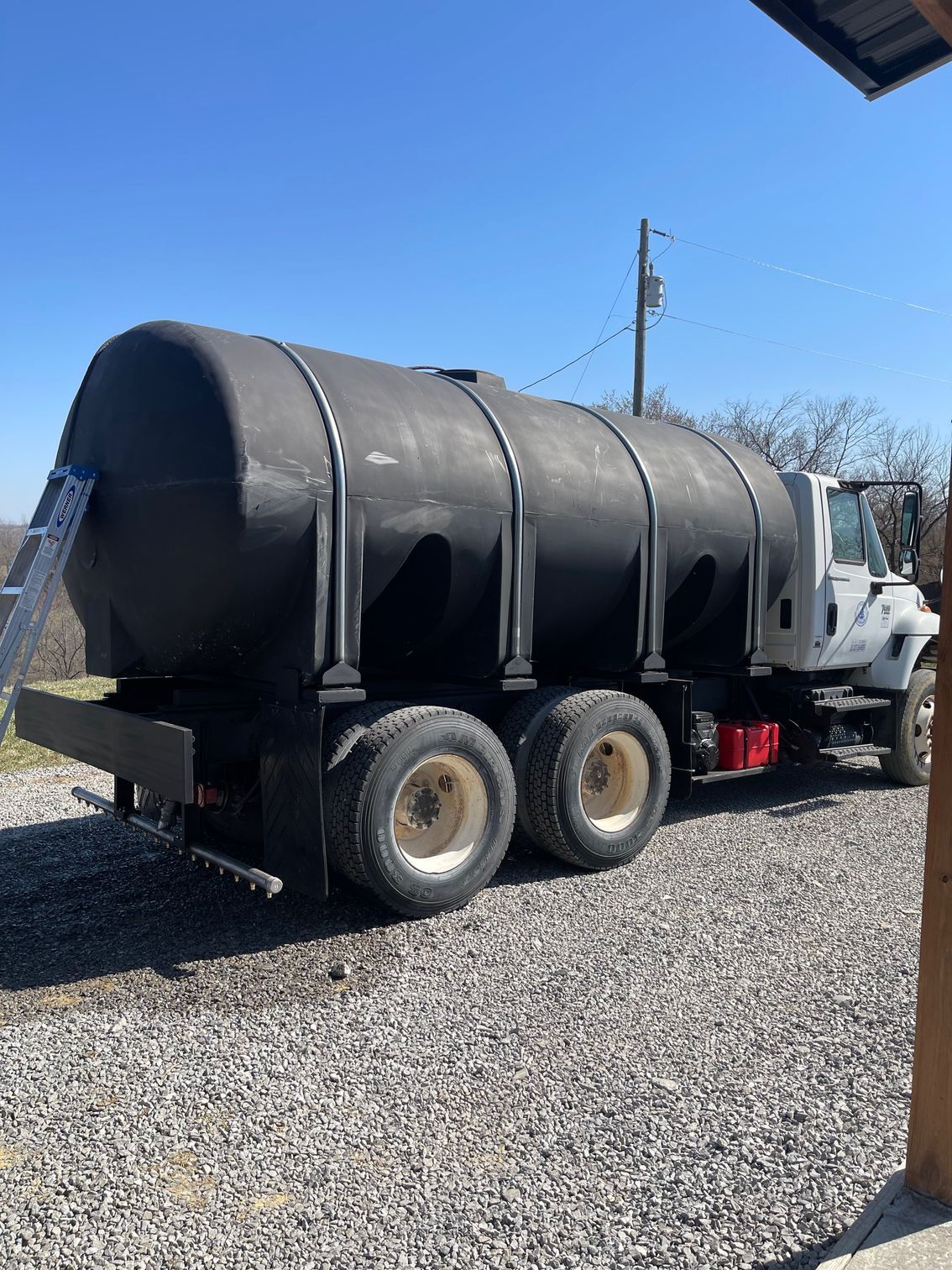 Black vacuum truck with silver cab parked on gravel under a blue sky