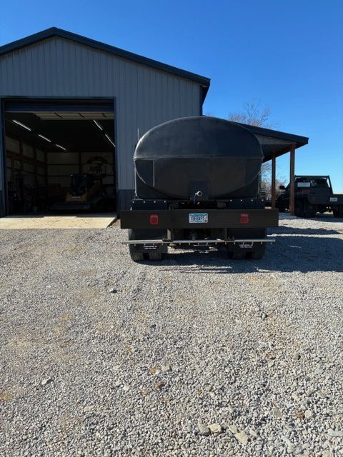 Black trailer parked on gravel in front of a metal workshop building.