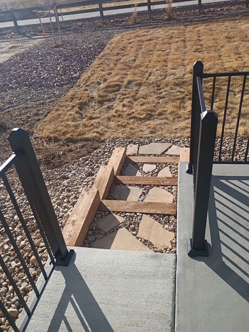 Entry steps leading to a yard, featuring a gravel base, wooden steps, and a railing.