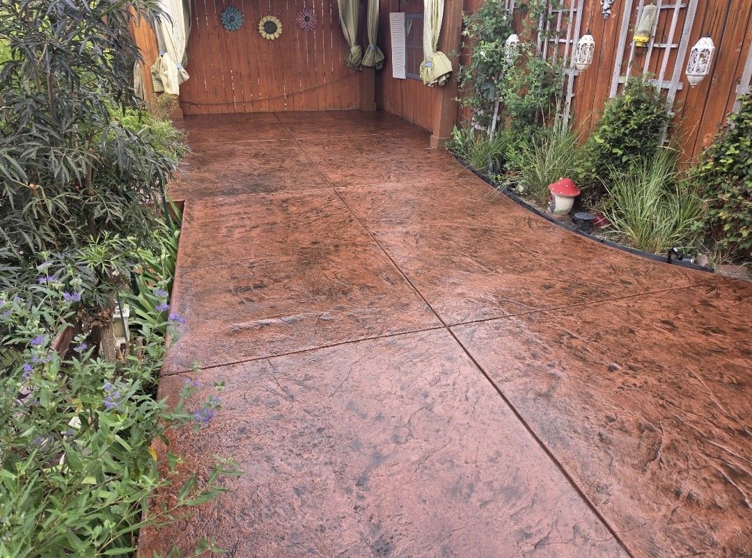 Wet red concrete driveway leading to a wooden gate, bordered by plants and brick walls