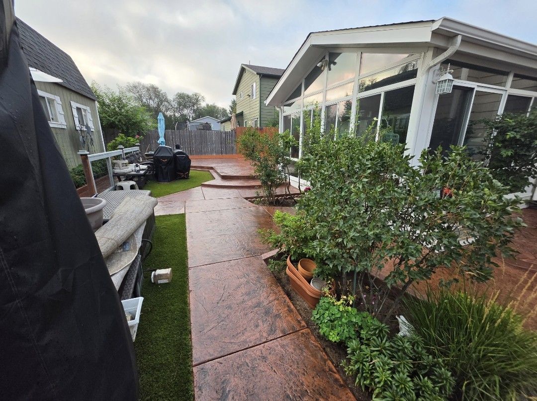 Rainy suburban side yard with wet walkway, potted plants, and a covered porch.