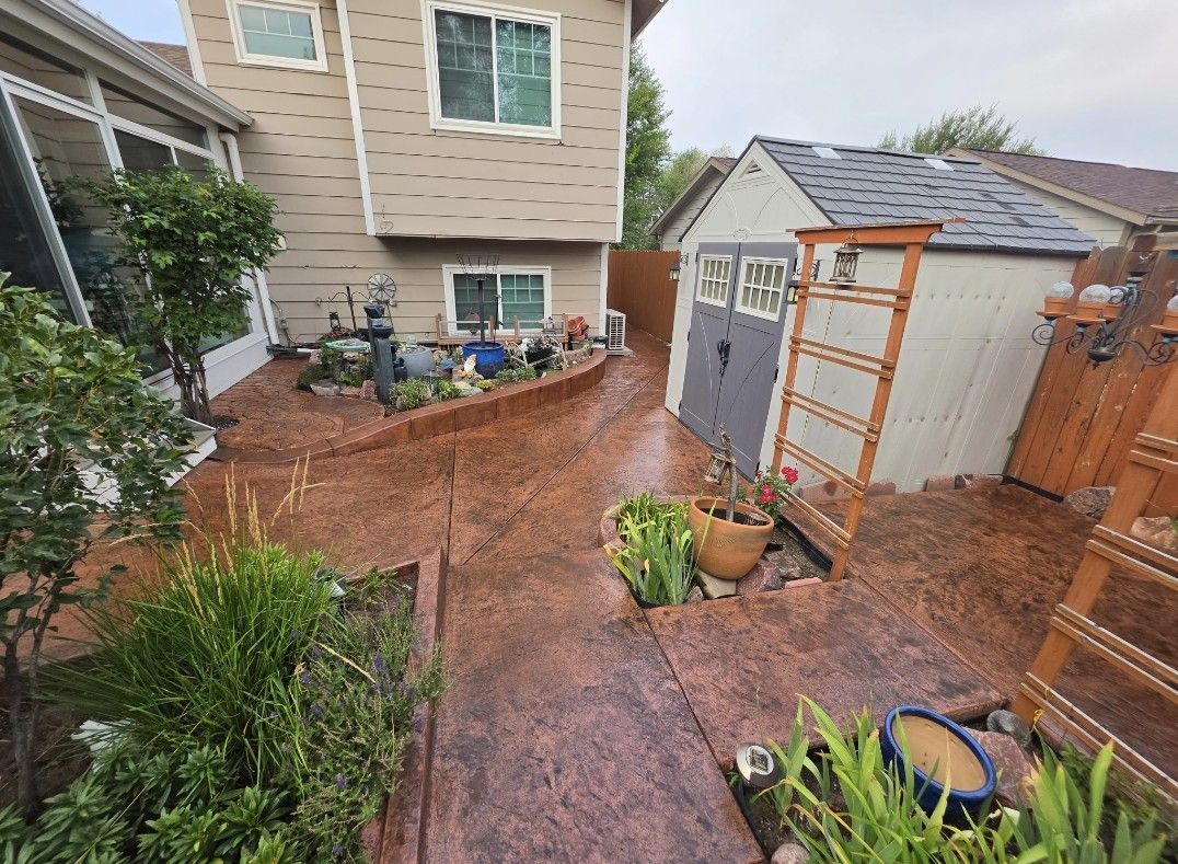 Small backyard with wooden deck, brick patio, plants, and a shed beside a house