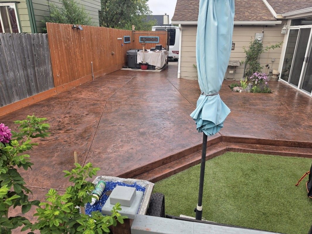 Backyard patio with wet wooden deck, lawn, patio umbrella, and a barbecue grill near the fence