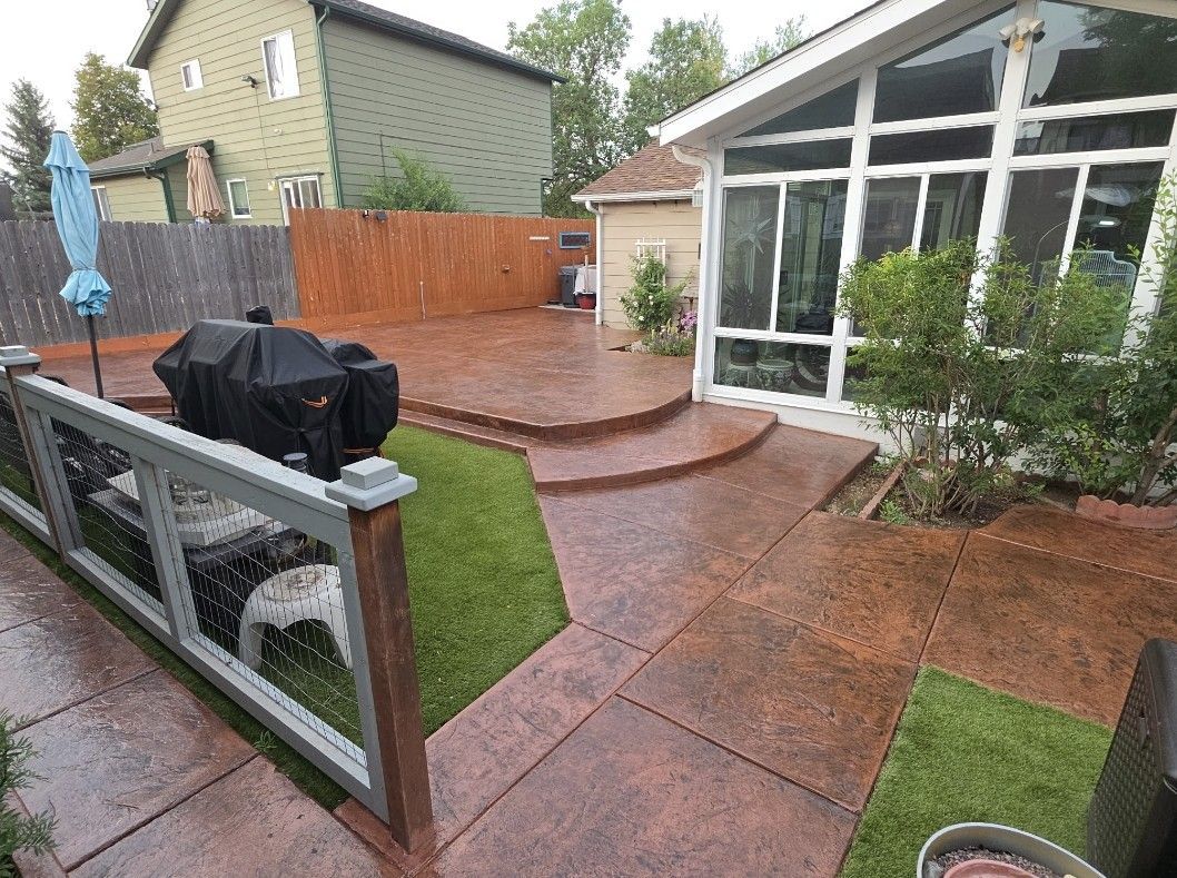 Rainy backyard patio with red stamped concrete, steps, lawn, covered grill, and a glass sunroom