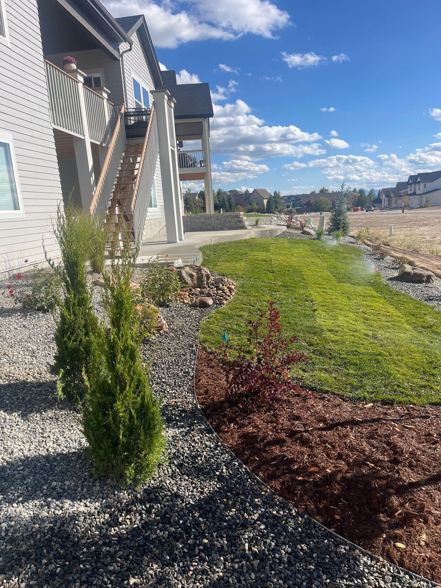 Building exterior with landscaping; green grass, mulch, and small trees under a blue sky.