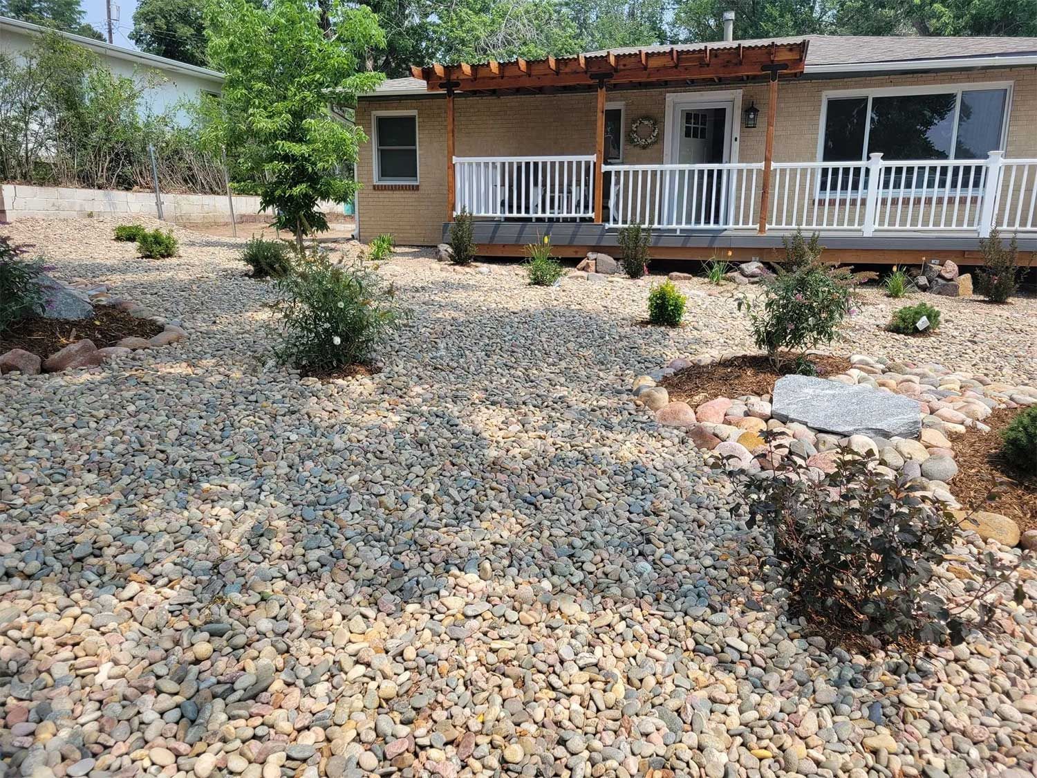 A house with a gravel front yard, small plants, and a deck with white railings.