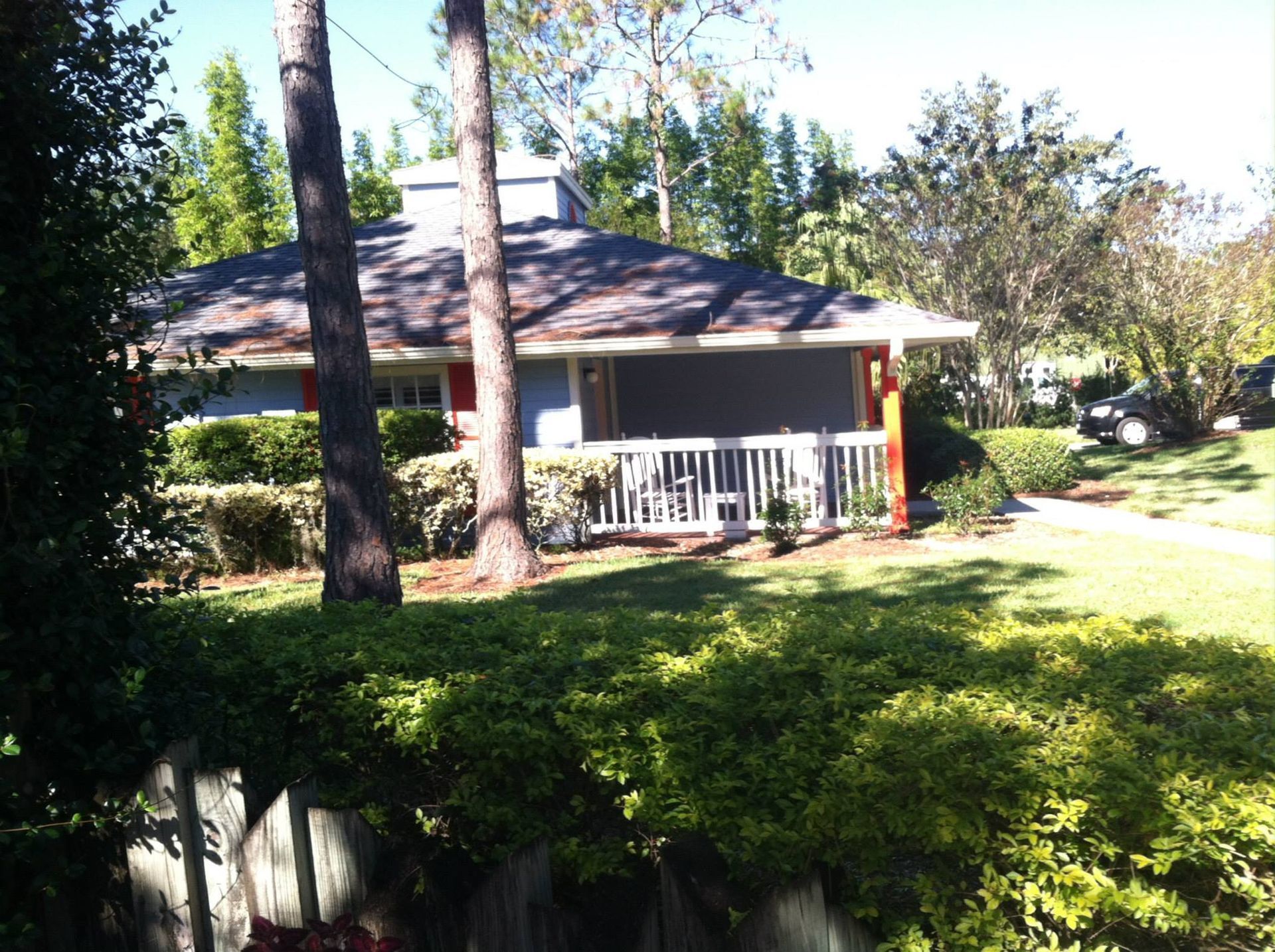 Small blue house with white porch, red door, and lush green landscaping.