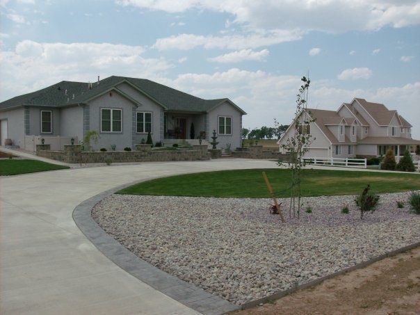 Two houses with driveways and landscaping under a blue sky.