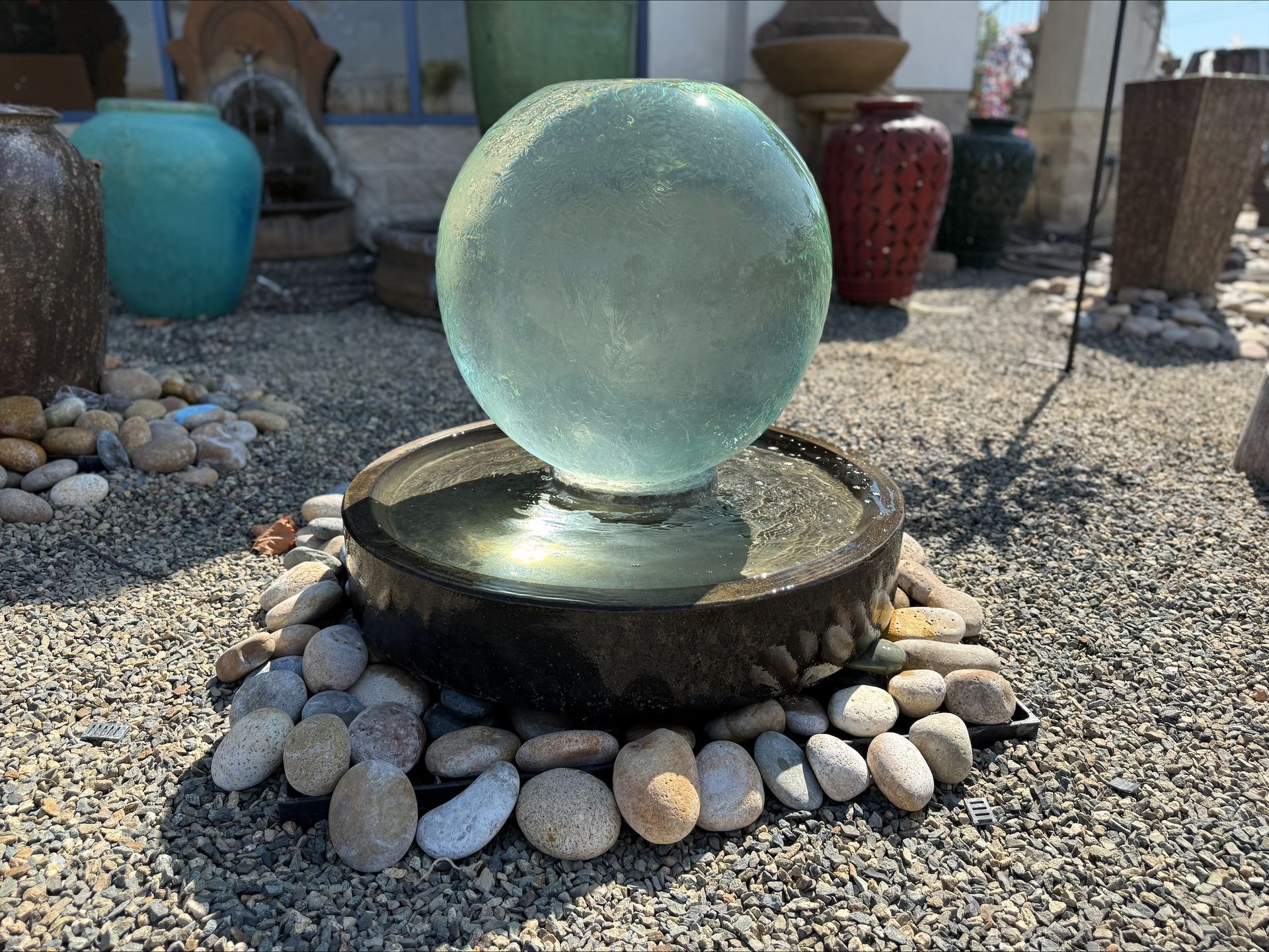 A glass ball is sitting on top of a fountain surrounded by rocks.