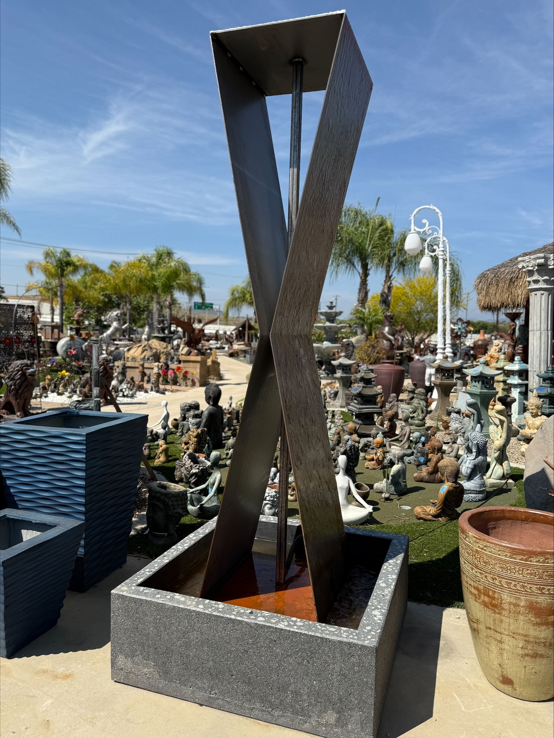 A large fountain is sitting in a garden surrounded by potted plants.