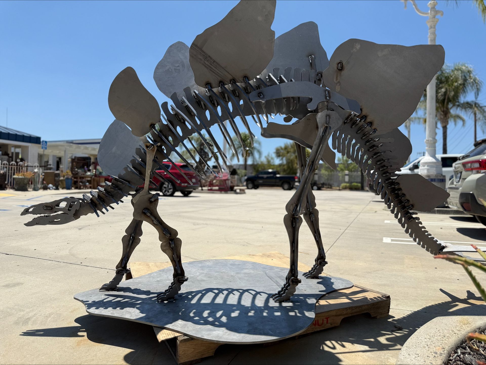 A statue of a dinosaur is sitting on a pallet in a parking lot.