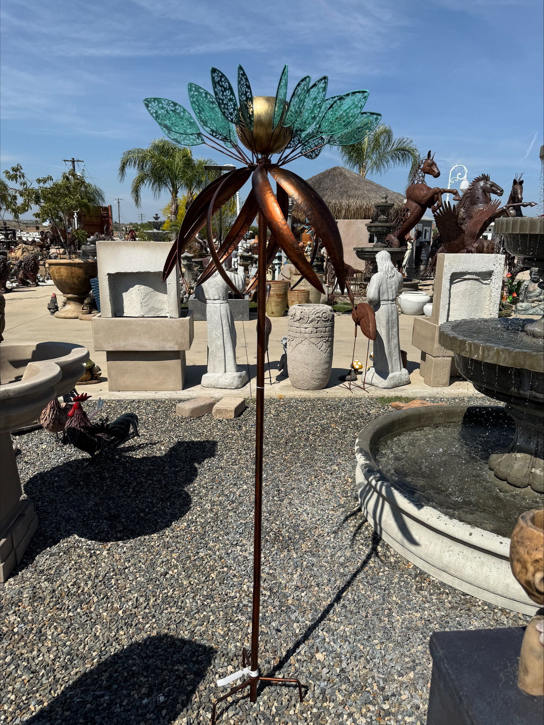 A statue of a palm tree is sitting in a gravel area next to a fountain.