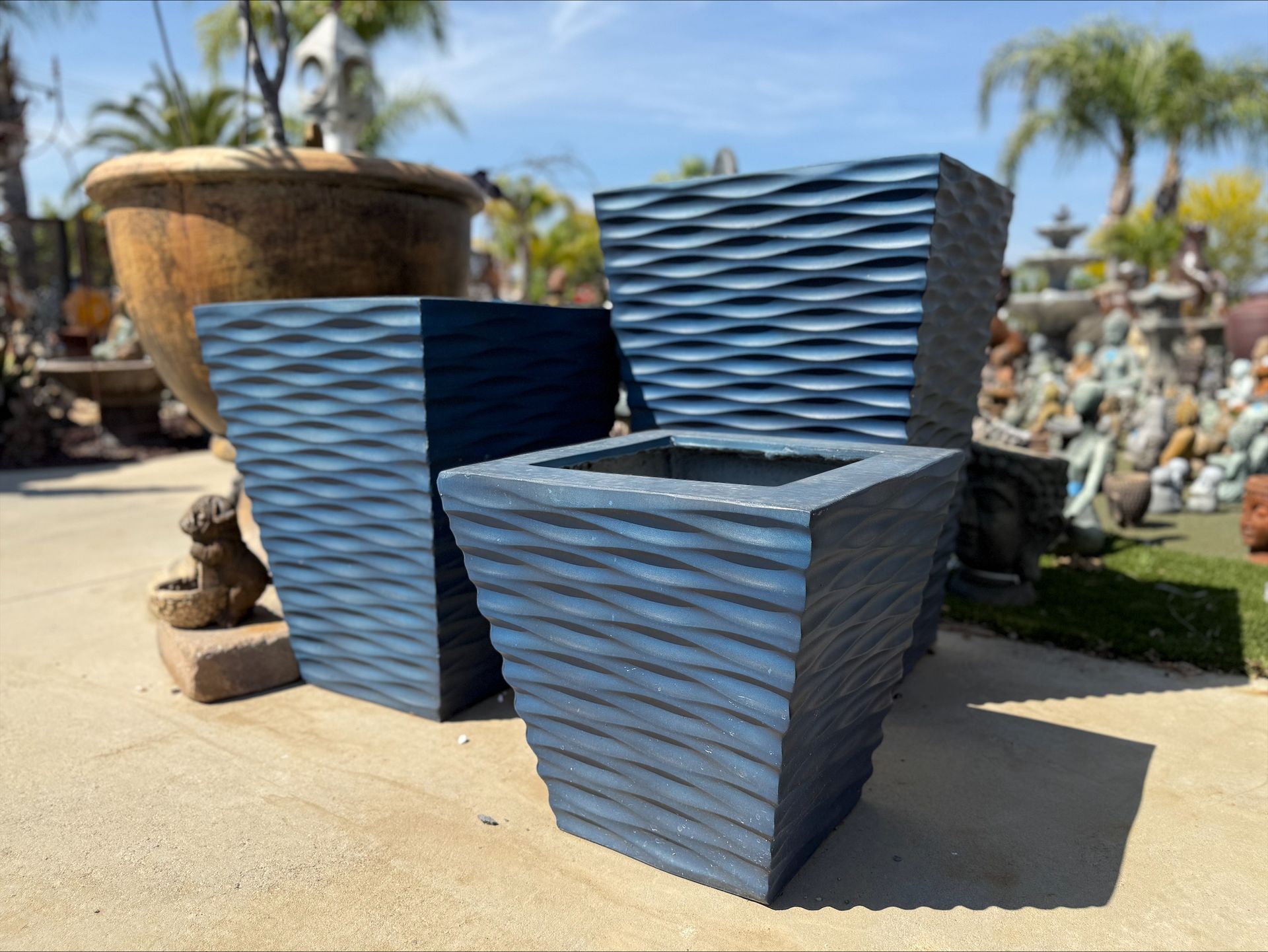 Three blue planters are sitting next to each other on a sidewalk.